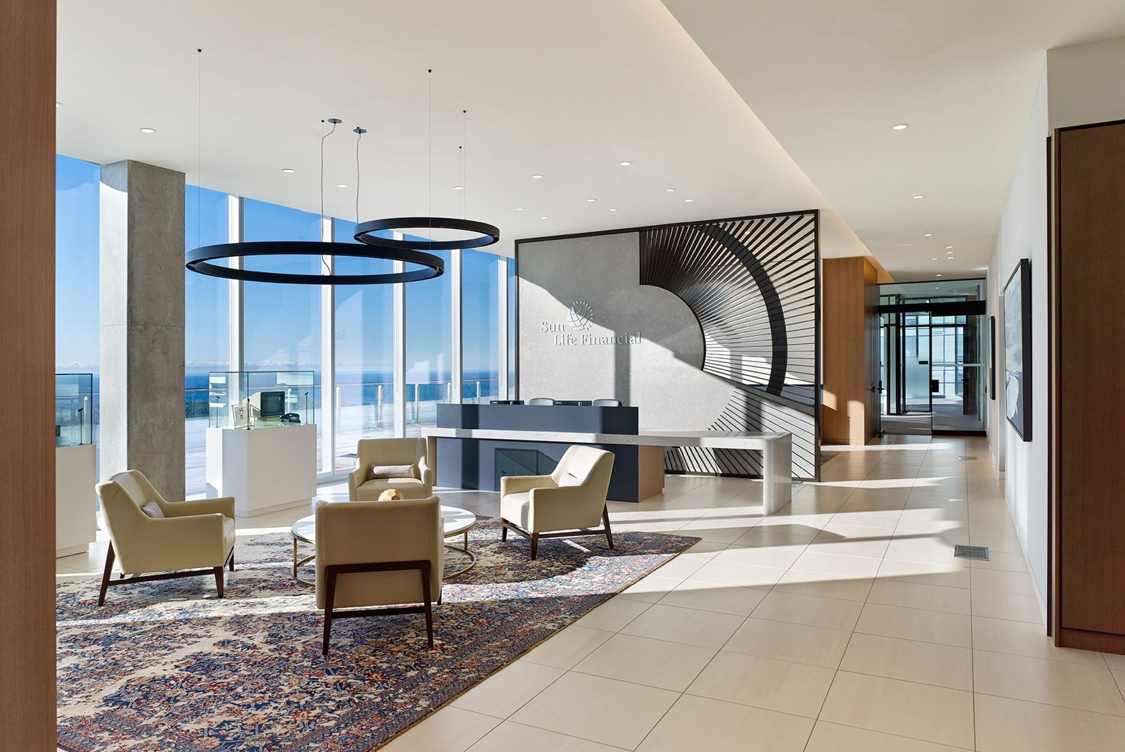 Reception lounge with armchairs and a sculptural screen by tall windows