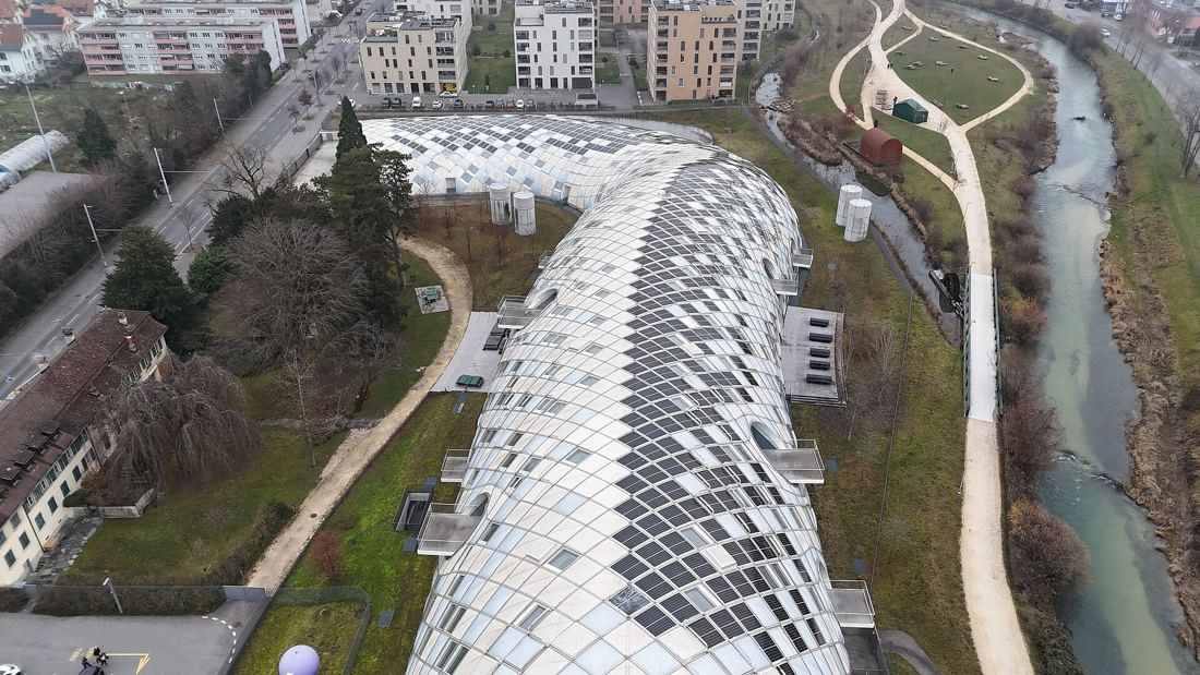 The Swatch Group: Aerial view of the curved building beside a river and park paths