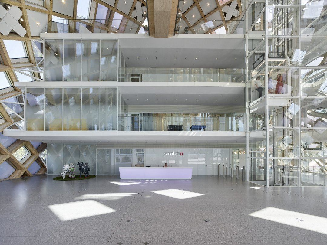 The Swatch Group: Bright atrium with a long white reception desk and stacked glass-fronted galleries under a wooden lattice