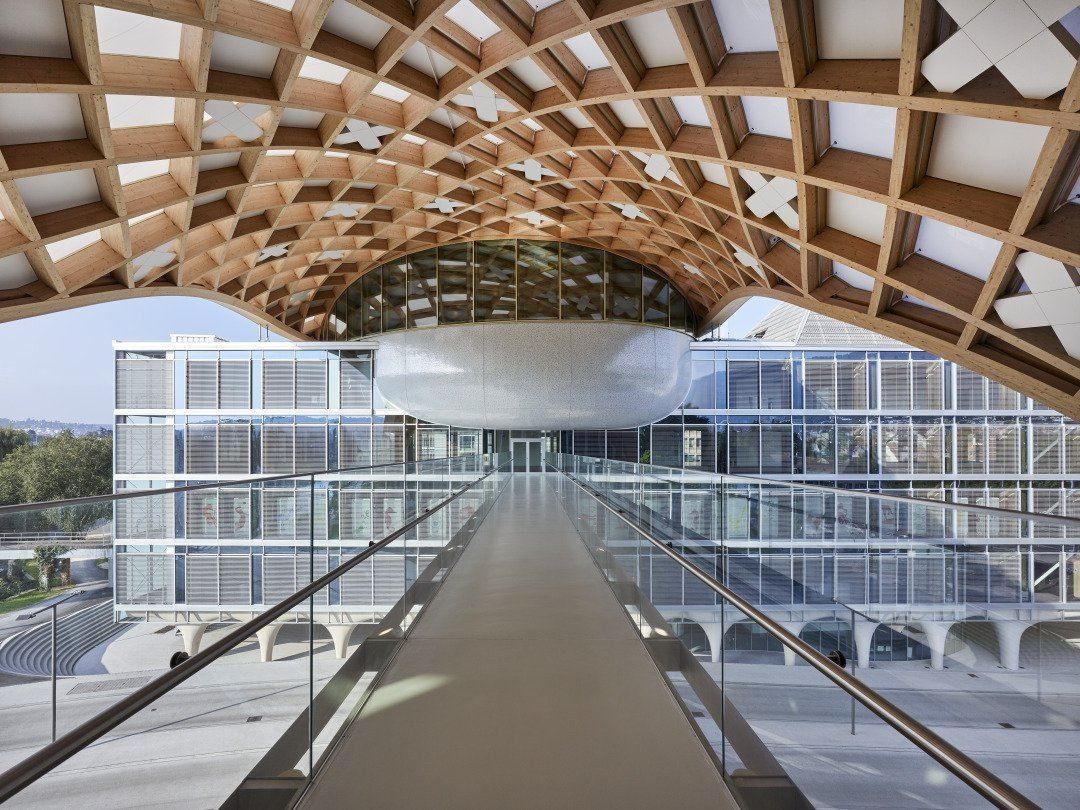 The Swatch Group: Covered footbridge running beneath a timber lattice towards a glass building with a silver oval volume