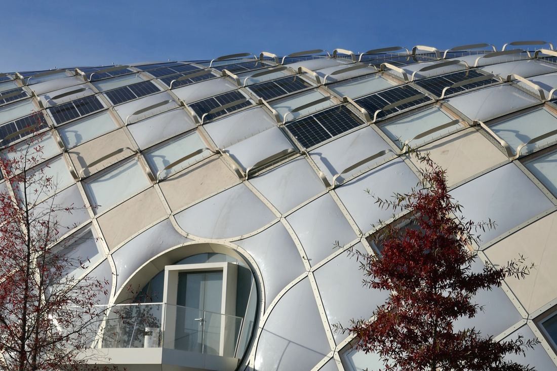 The Swatch Group: Curved façade with solar panels and a round balcony opening, autumn trees in front
