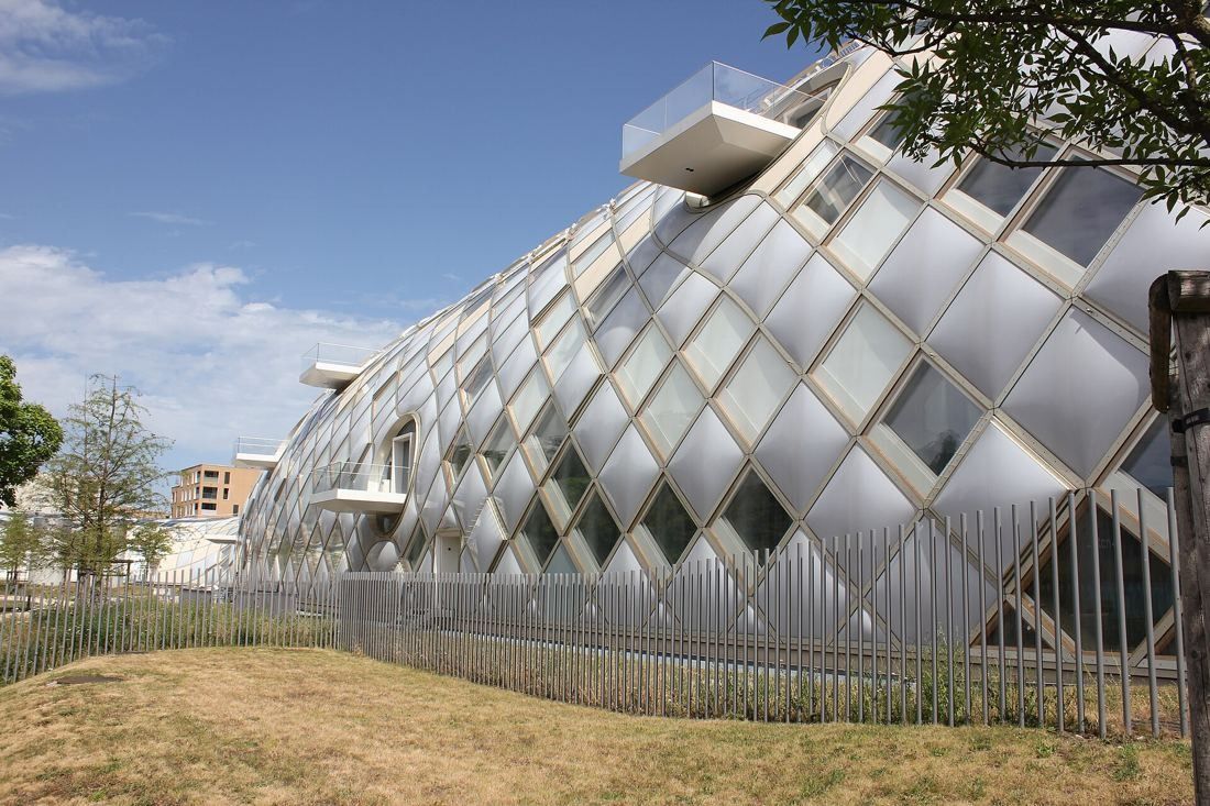 The Swatch Group: Diamond-patterned curved façade with a small balcony, seen from a lawn