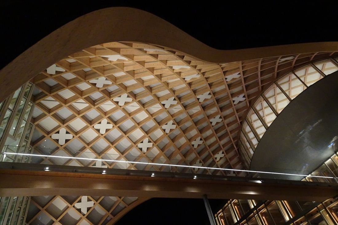 The Swatch Group: Lit timber lattice with white cross panels curving around a silver oval form at night