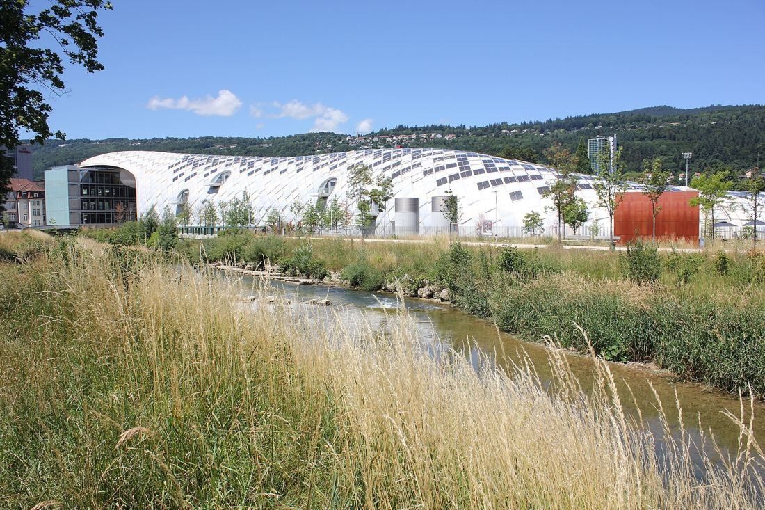 The Swatch Group: Long white curved building seen across a river with tall grass in the foreground