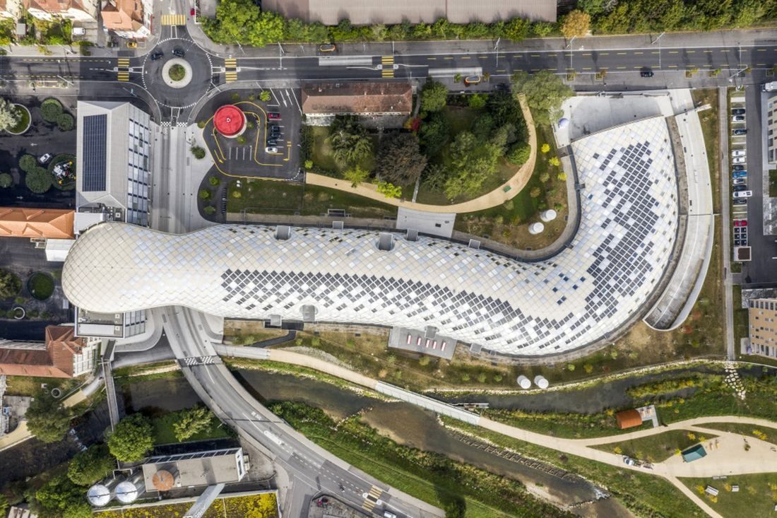 The Swatch Group: Overhead aerial view of a long curved white roof with solar panels, surrounded by greenery and a river