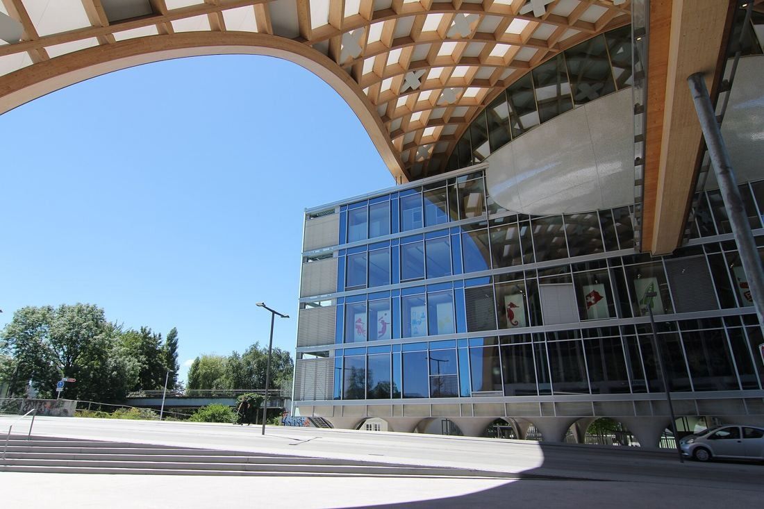 The Swatch Group: Timber grid arch ending above a street, next to a glass building with a suspended silver oval