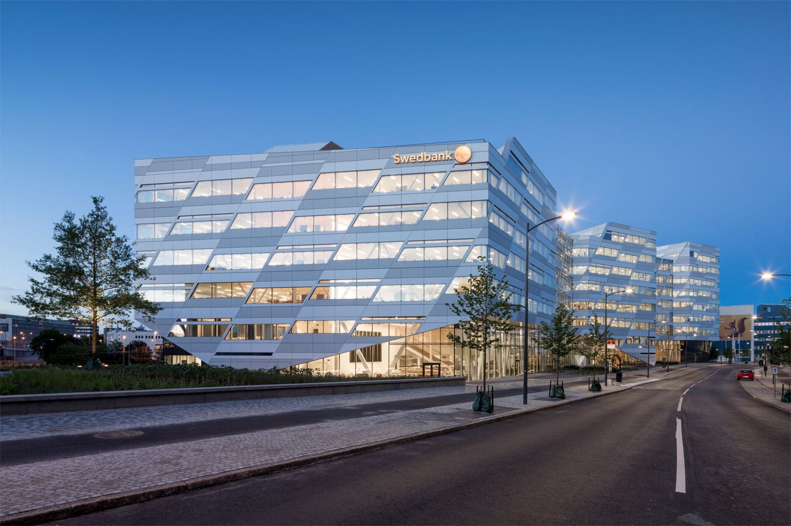 A long glass office building lit at dusk beside a street