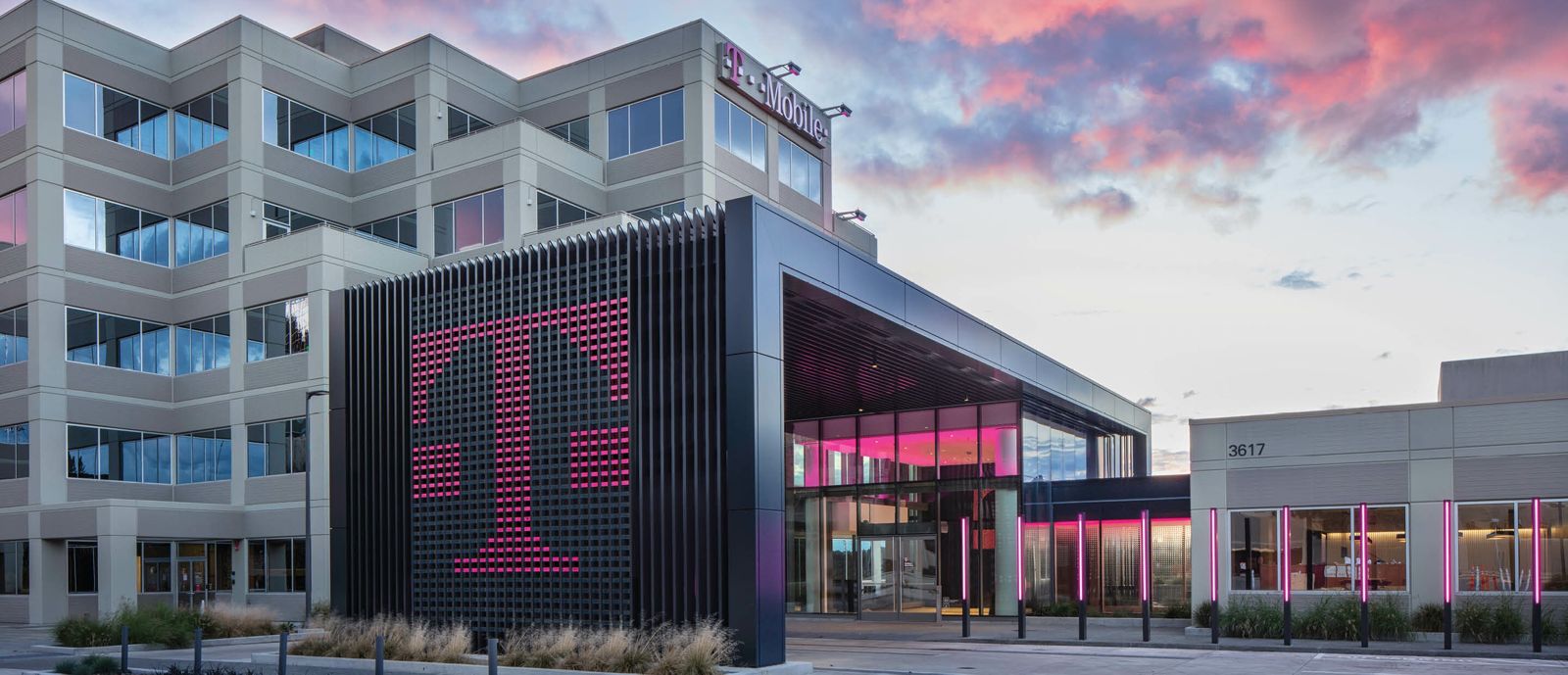Office building with a large magenta T sign on a dark entrance pavilion at dusk