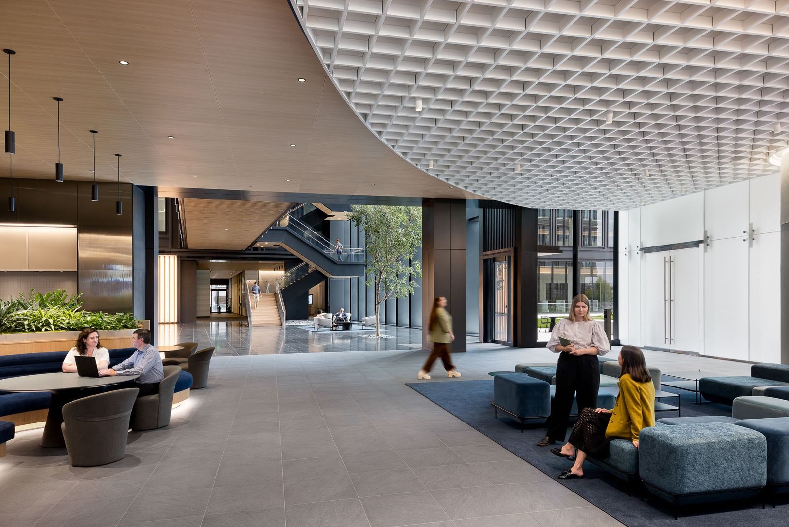A double-height lobby with a sweeping coffered ceiling, lounge seating and a monumental stair beyond