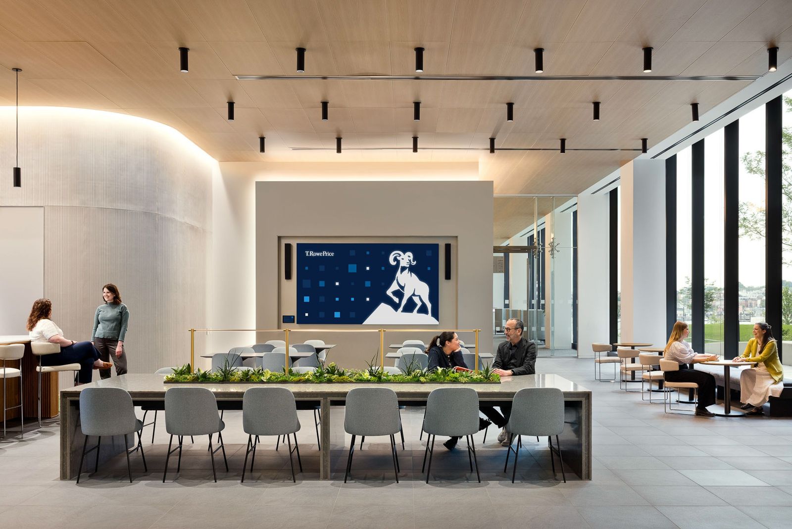 T. Rowe Price: A long shared table under spotlights in front of a wall screen