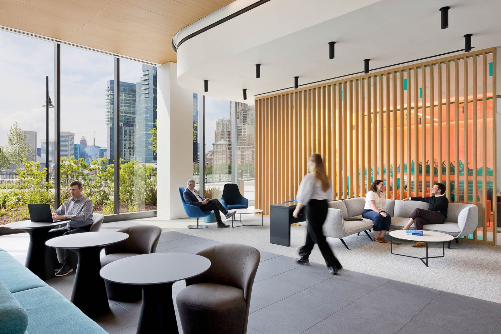 T. Rowe Price: A lounge with timber slats and round tables beside tall windows over the harbor