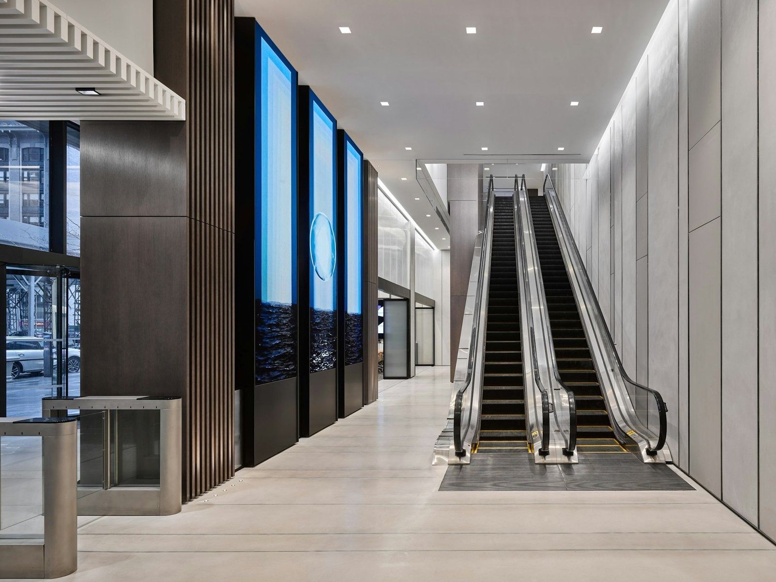 Tall lobby with a pair of escalators beside a wall of vertical video screens