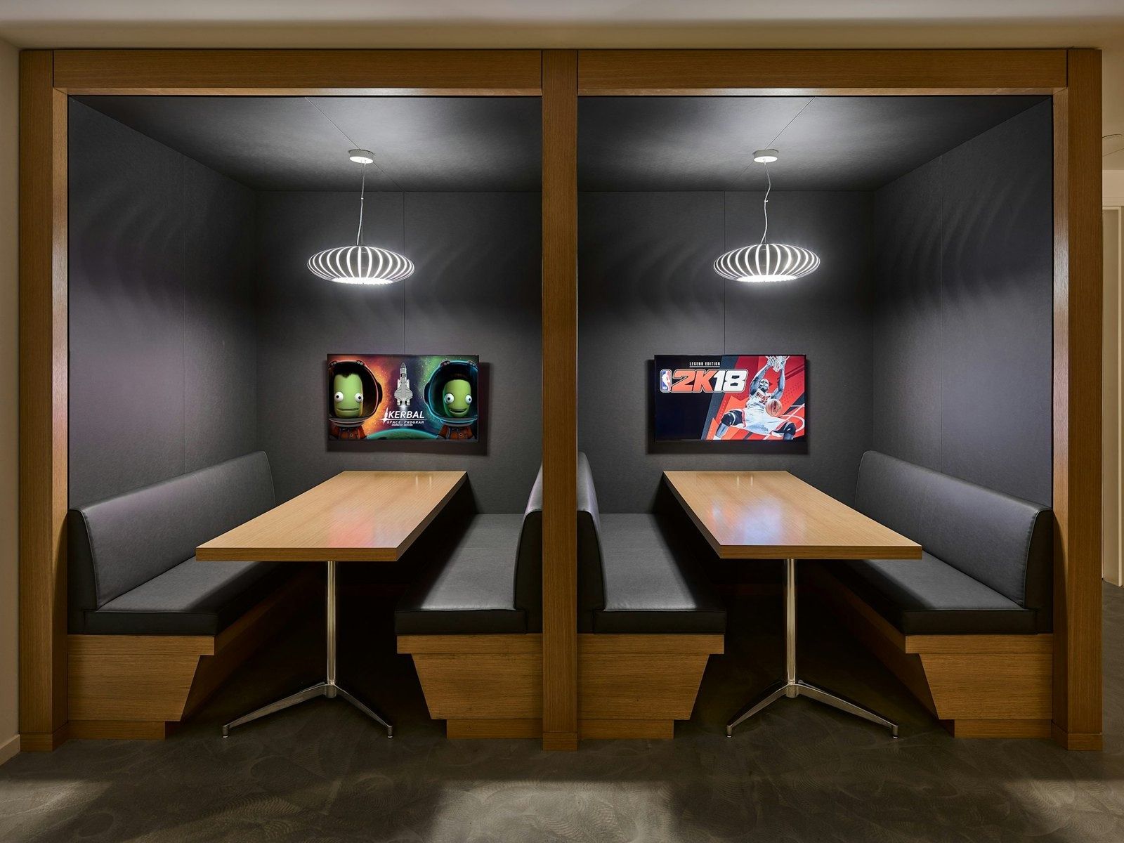Take-Two Interactive: Two dark wood booths with tables, pendant lamps and game screens on the wall