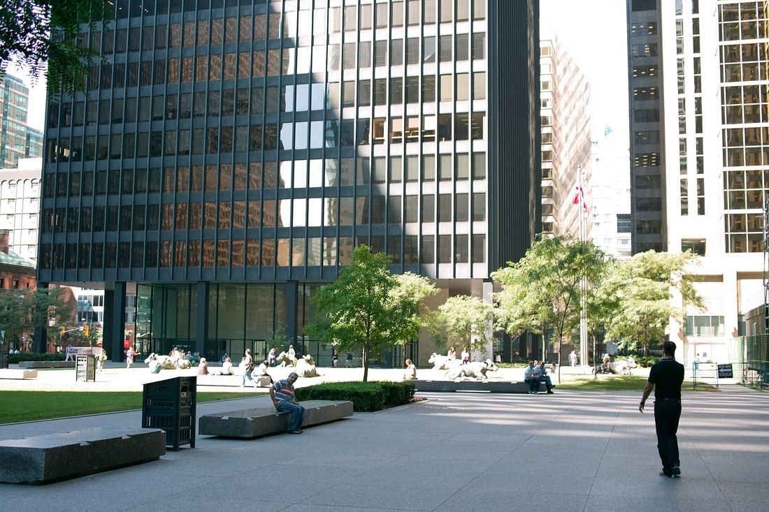 TD Bank Group (The Toronto-Dominion Bank): Granite plaza with lawn, trees and benches at the base of a black tower