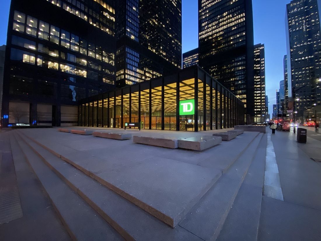 TD Bank Group (The Toronto-Dominion Bank): Low glass pavilion lit at dusk on a granite plaza between dark towers