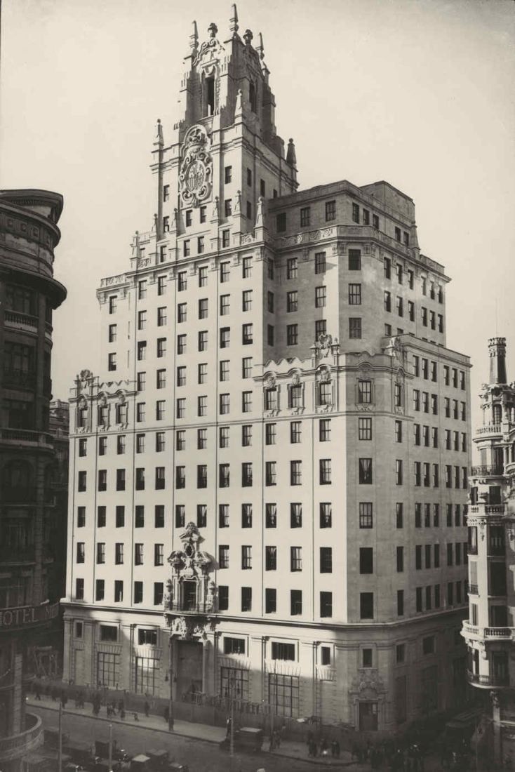 Black-and-white photo of a tall stone building with an ornate tower on a city corner