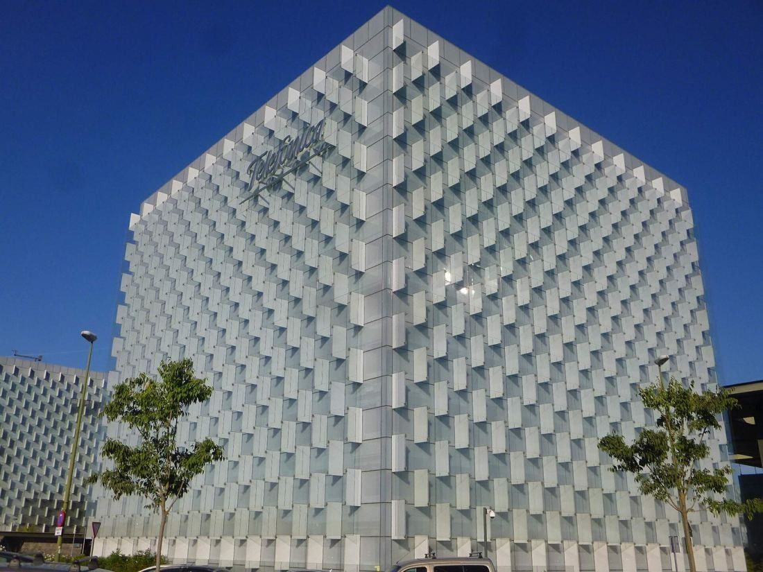 Telefónica: Close view of a glass tower with stepped facade panels and small trees