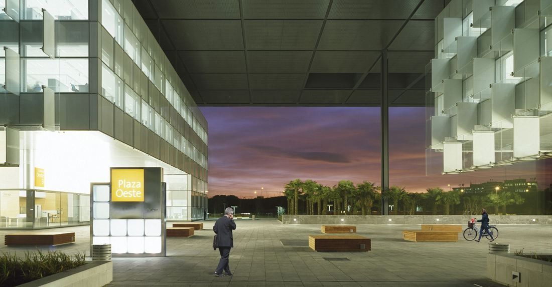 Telefónica: Covered plaza with benches opening onto a sunset sky, a few distant people walking