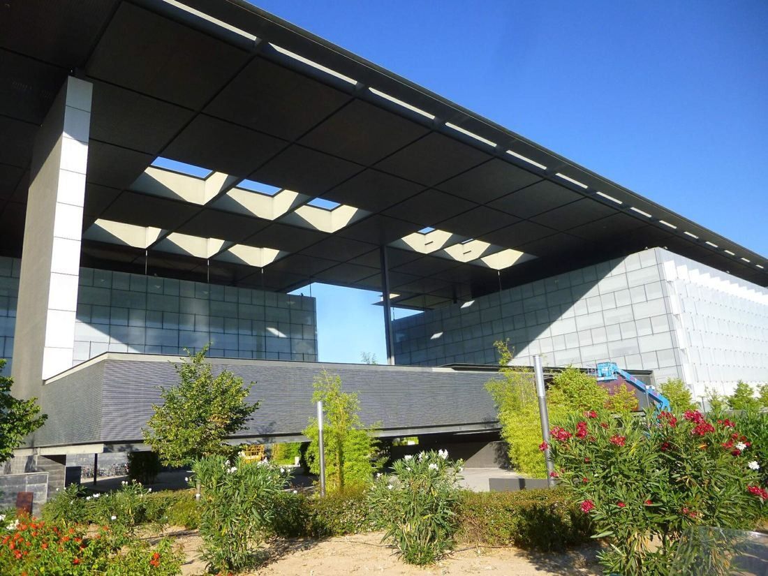 Telefónica: Dark canopy with skylight cut-outs over glass buildings and red flowers