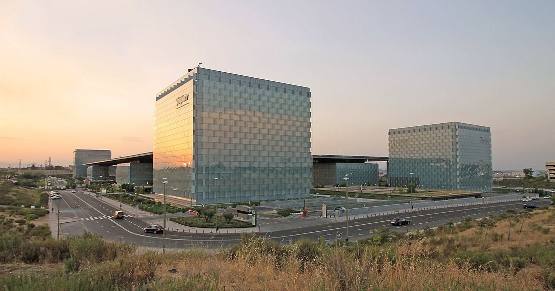 Telefónica: Glass towers and campus buildings beside a curving road in evening light