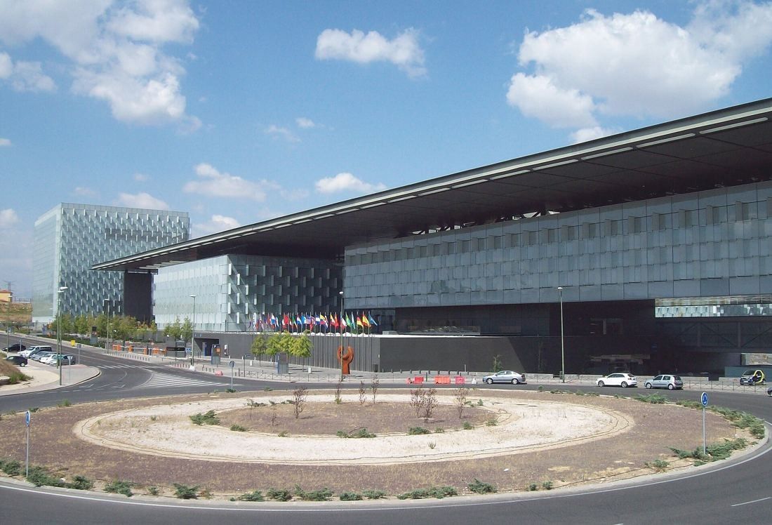 Telefónica: Long building under a deep canopy with flags in front of a roundabout