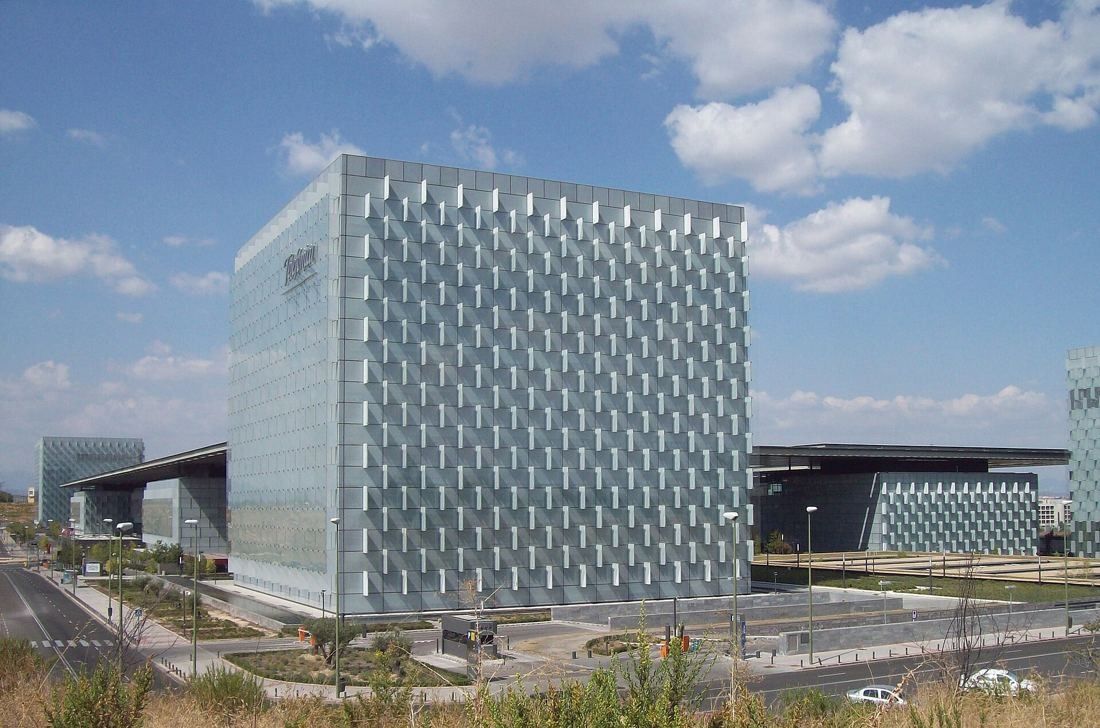 Telefónica: Square glass tower with a faceted facade next to low campus buildings