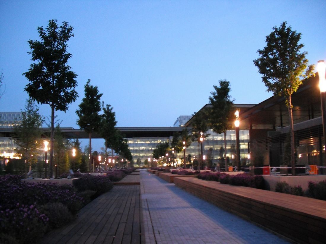 Telefónica: Tree-lined path with lamps leading toward low buildings at dusk