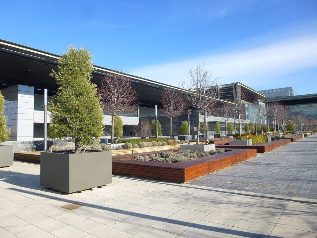 Telefónica: Wide paved square with planters and trees under a long roof edge