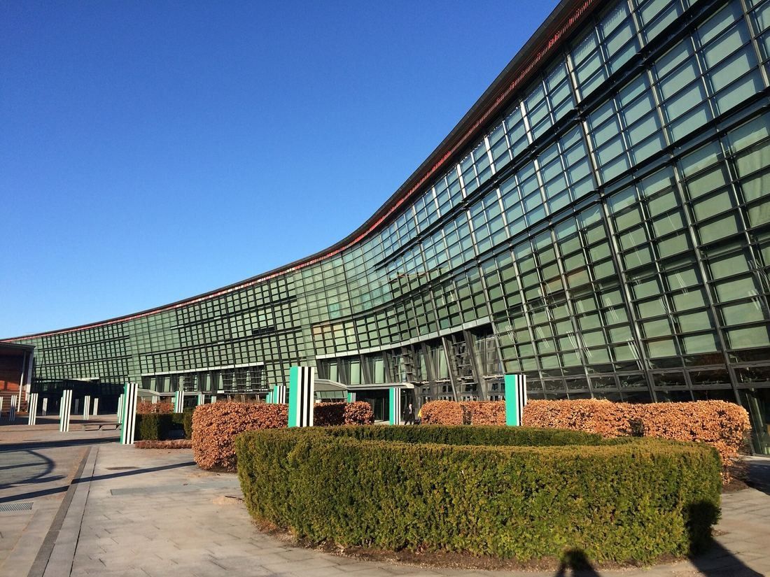 Telenor: Long curved glass facade with a round hedge in front under a blue sky