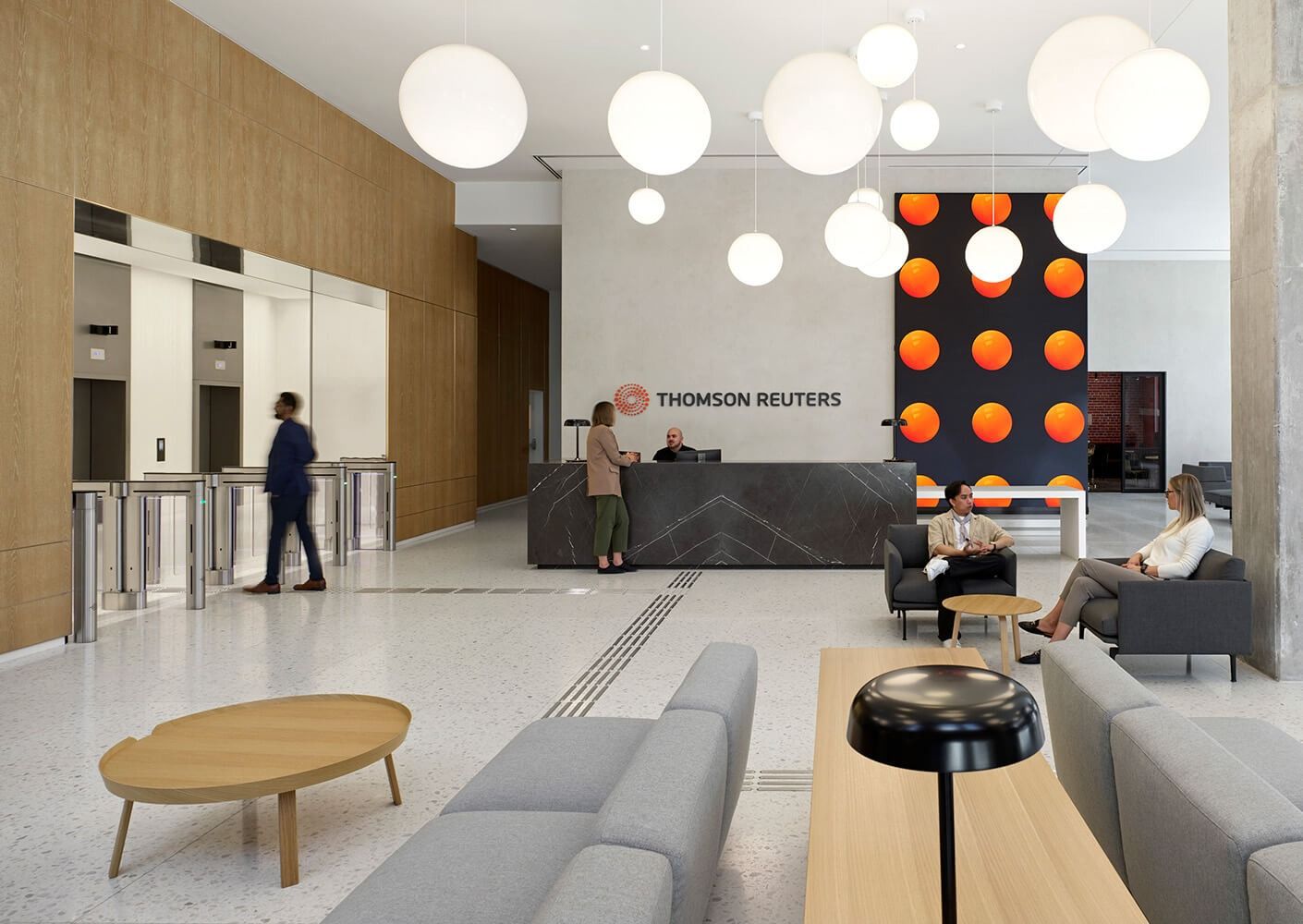 A bright reception with a wood-clad wall, white globe lights and the Thomson Reuters name behind the desk