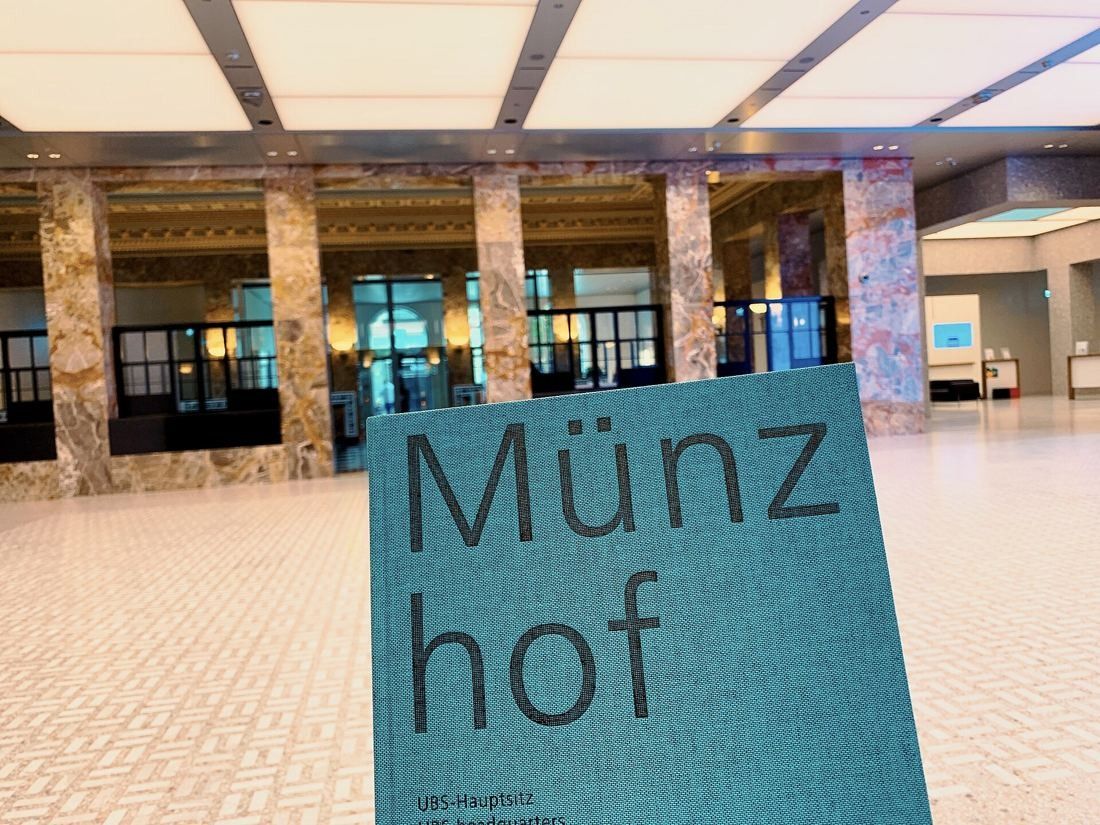 UBS: Bright hall with marble columns, a patterned floor and a luminous ceiling, a booklet titled Münzhof held in the foreground