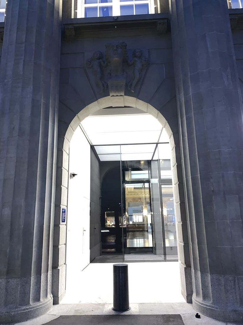 UBS: Glass entrance seen through a tall dark stone archway