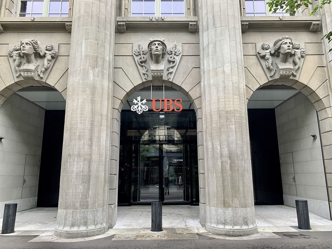 UBS: Glass entrance with the UBS sign between two massive stone columns with carved heads above