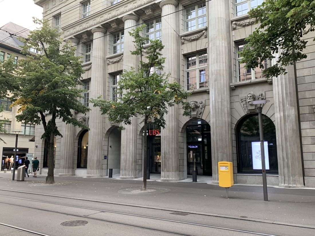 UBS: Long stone façade seen at an angle along a street with tram tracks and trees