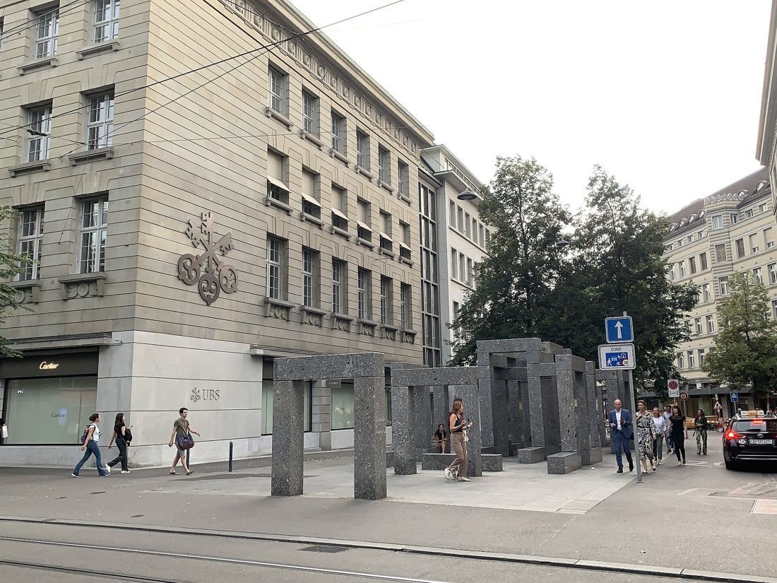 UBS: Plain stone corner of the building with a relief of three keys, stone column sculpture on the square in front