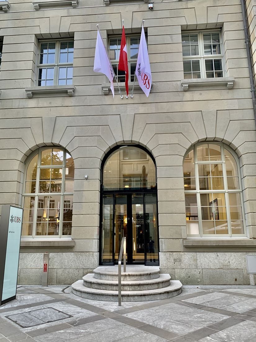 UBS: Stone façade with arched windows, steps to a glass door and flags above