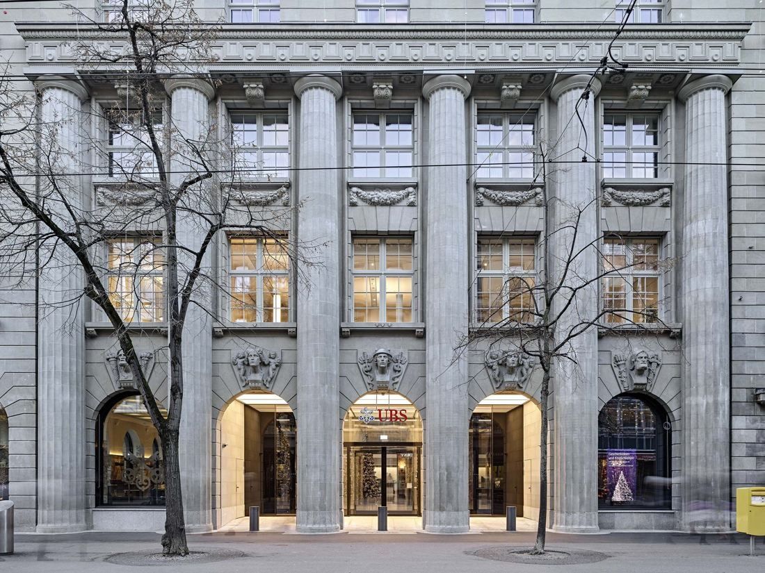 UBS: Symmetrical stone façade with tall columns and four lit arched openings at street level