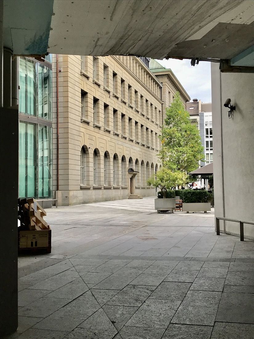 UBS: View from a covered passage into an open paved courtyard with a tree and stone façades