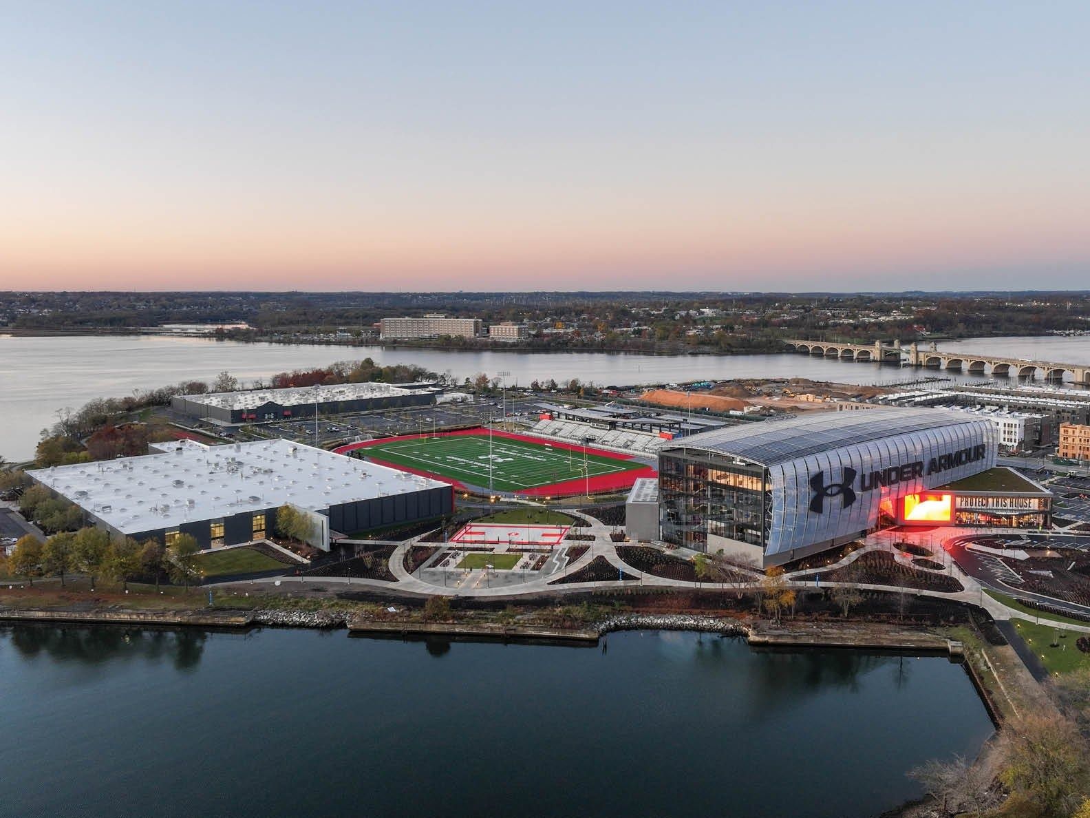 Under Armour: Aerial view at sunset of the waterfront campus with a stadium, red track and green field beside the water
