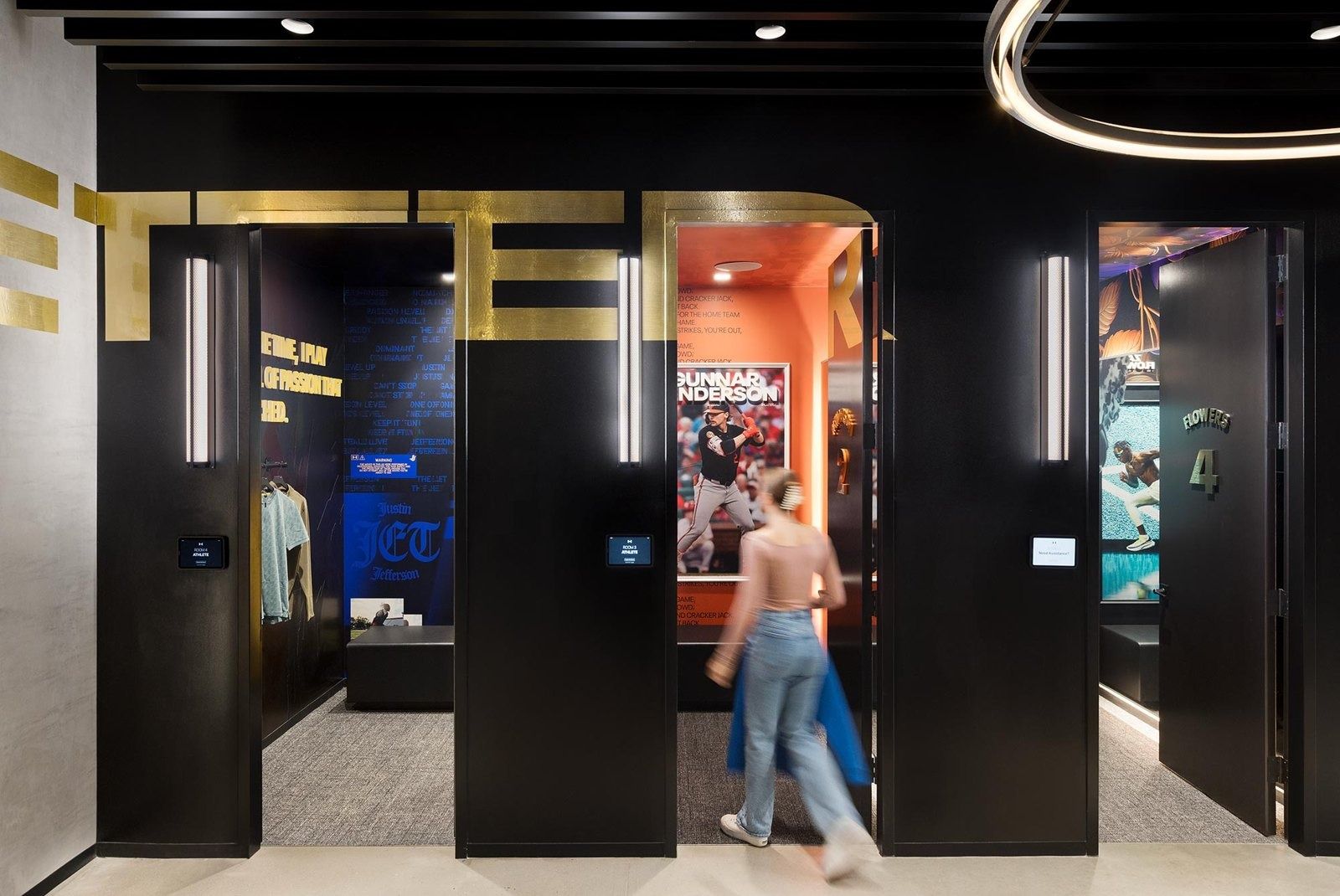 Under Armour: Black-framed doorways into small brightly coloured rooms with sports posters, a person walking past in motion blur