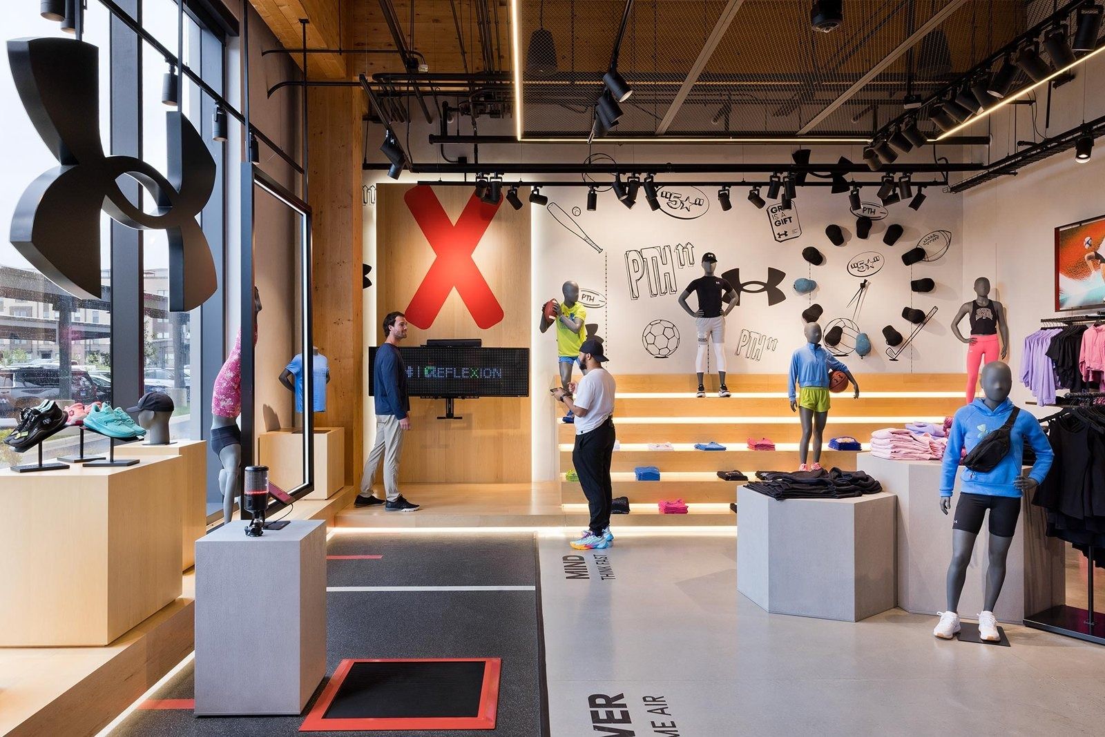 Under Armour: Display space with wooden walls, mannequins in sportswear on stepped platforms and a large red X graphic