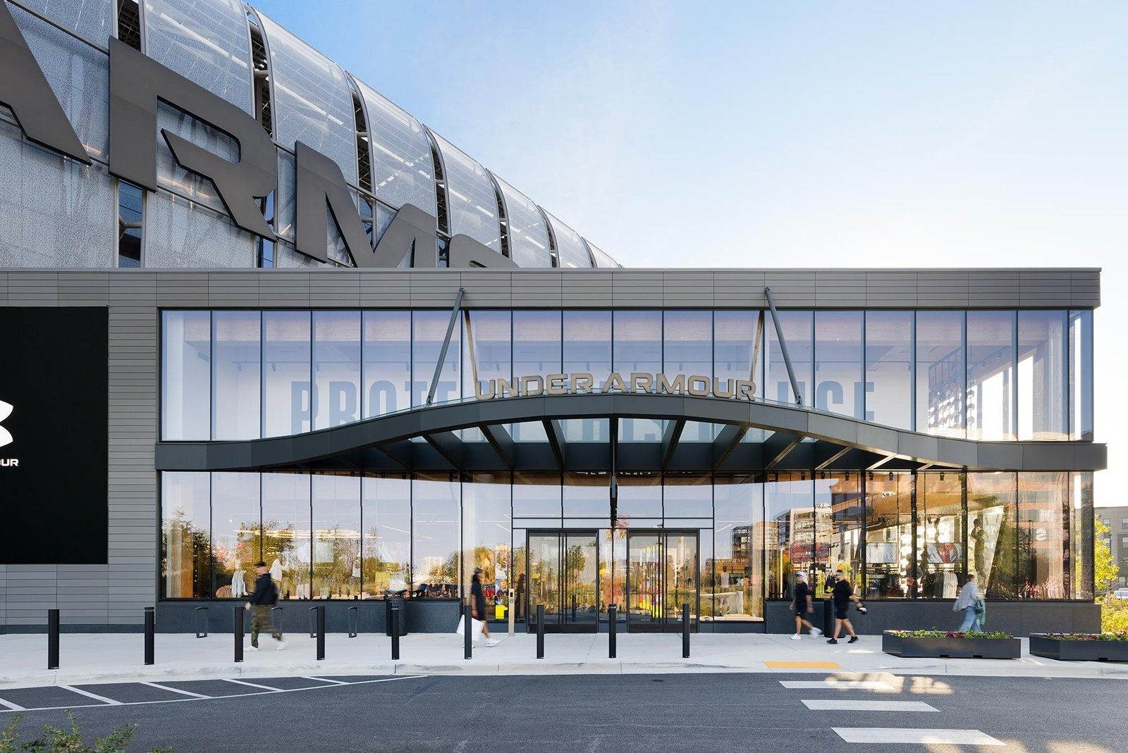 Under Armour: Glass entrance under a curved canopy with large lettering above, viewed from the car park