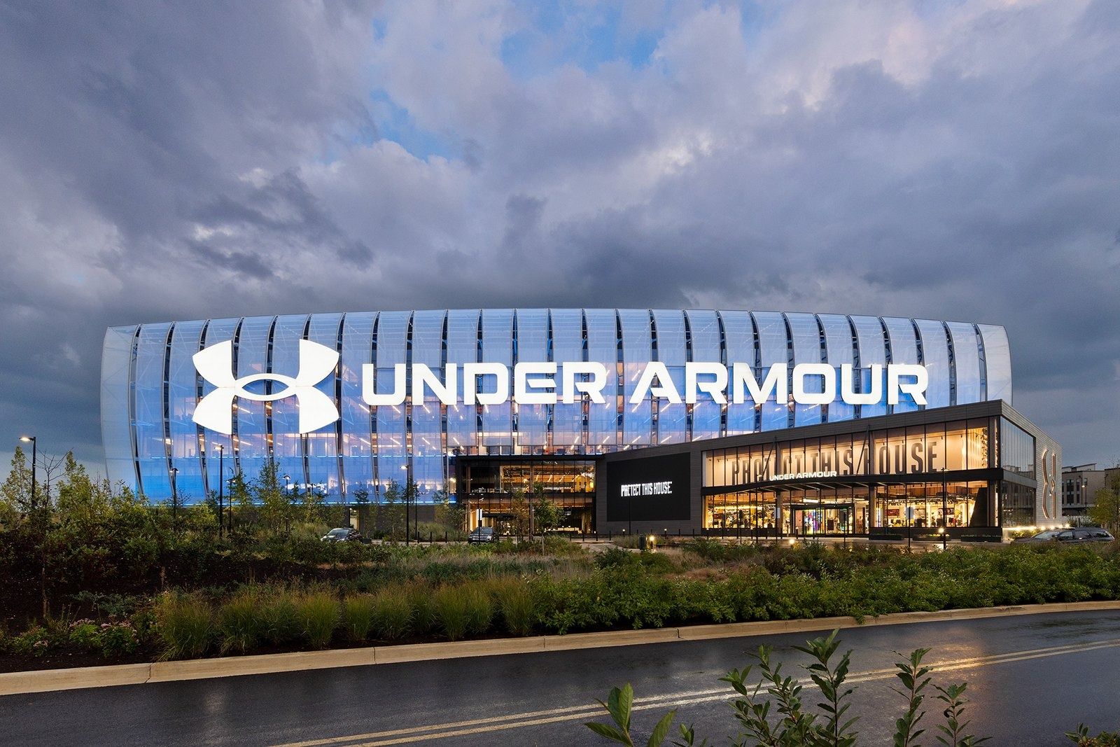 Under Armour: Glowing building with Under Armour lettering seen across water and greenery at dusk