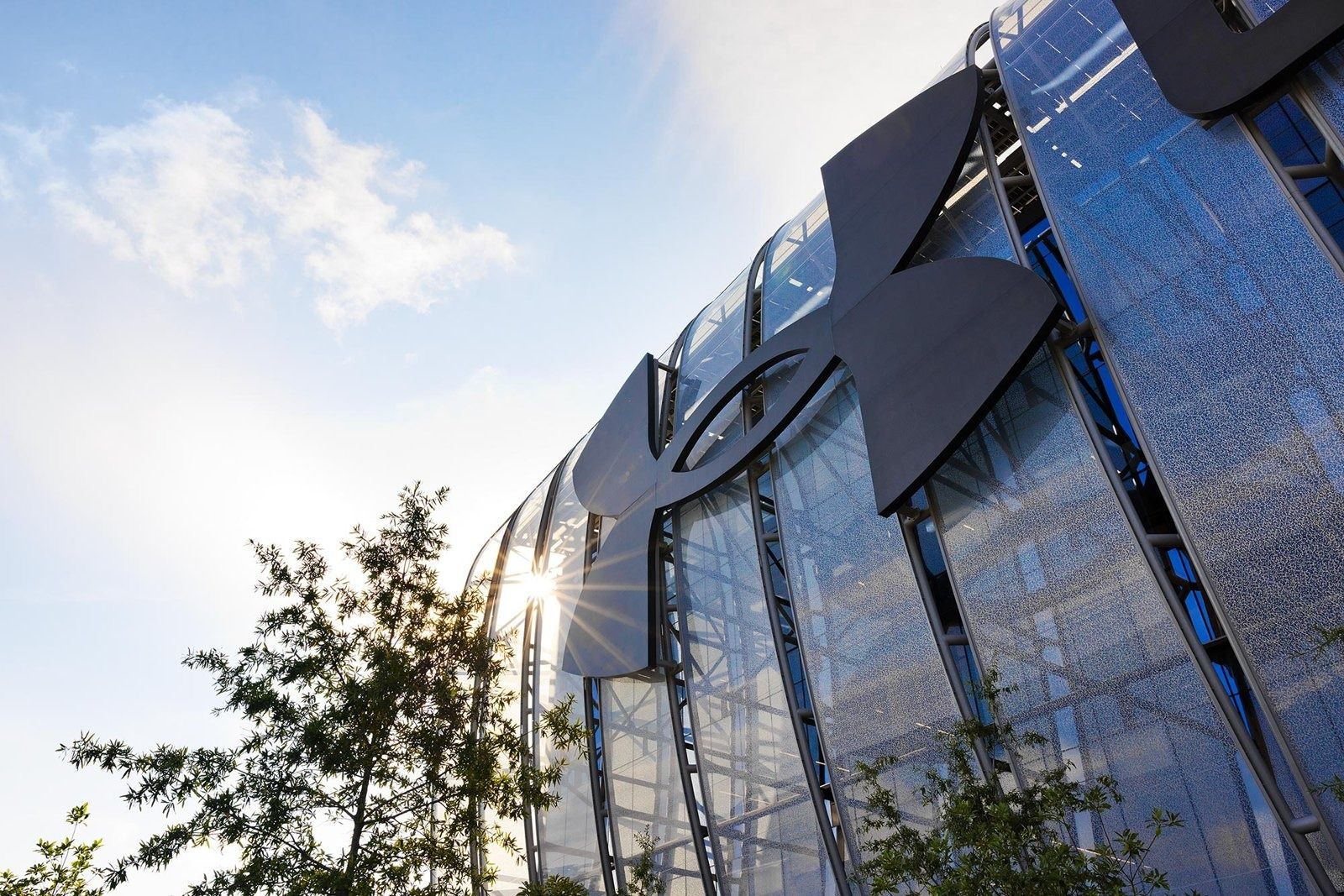 Under Armour: Looking up at a curved glass facade with a large logo, trees in the foreground and blue sky