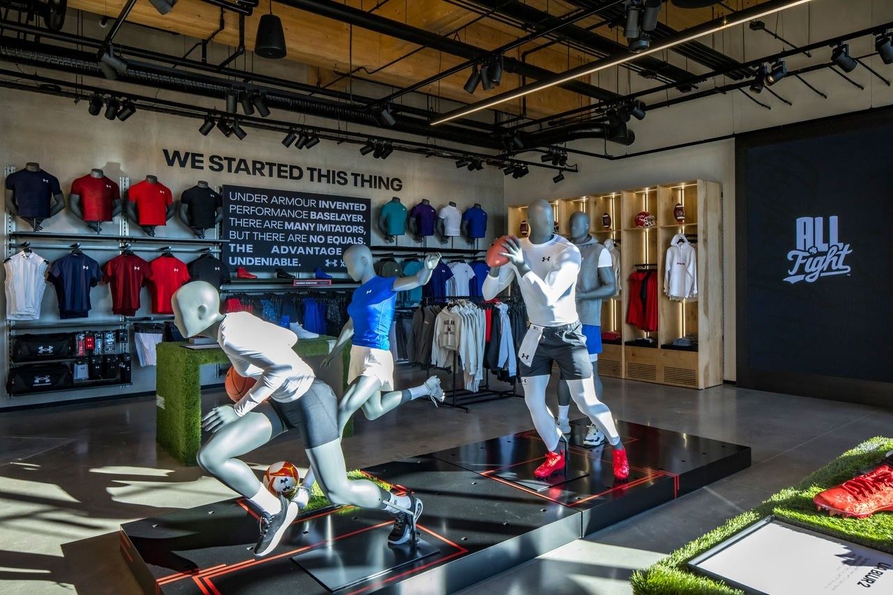 Under Armour: Mannequins in action poses on a platform in front of a wall of shirts and jerseys