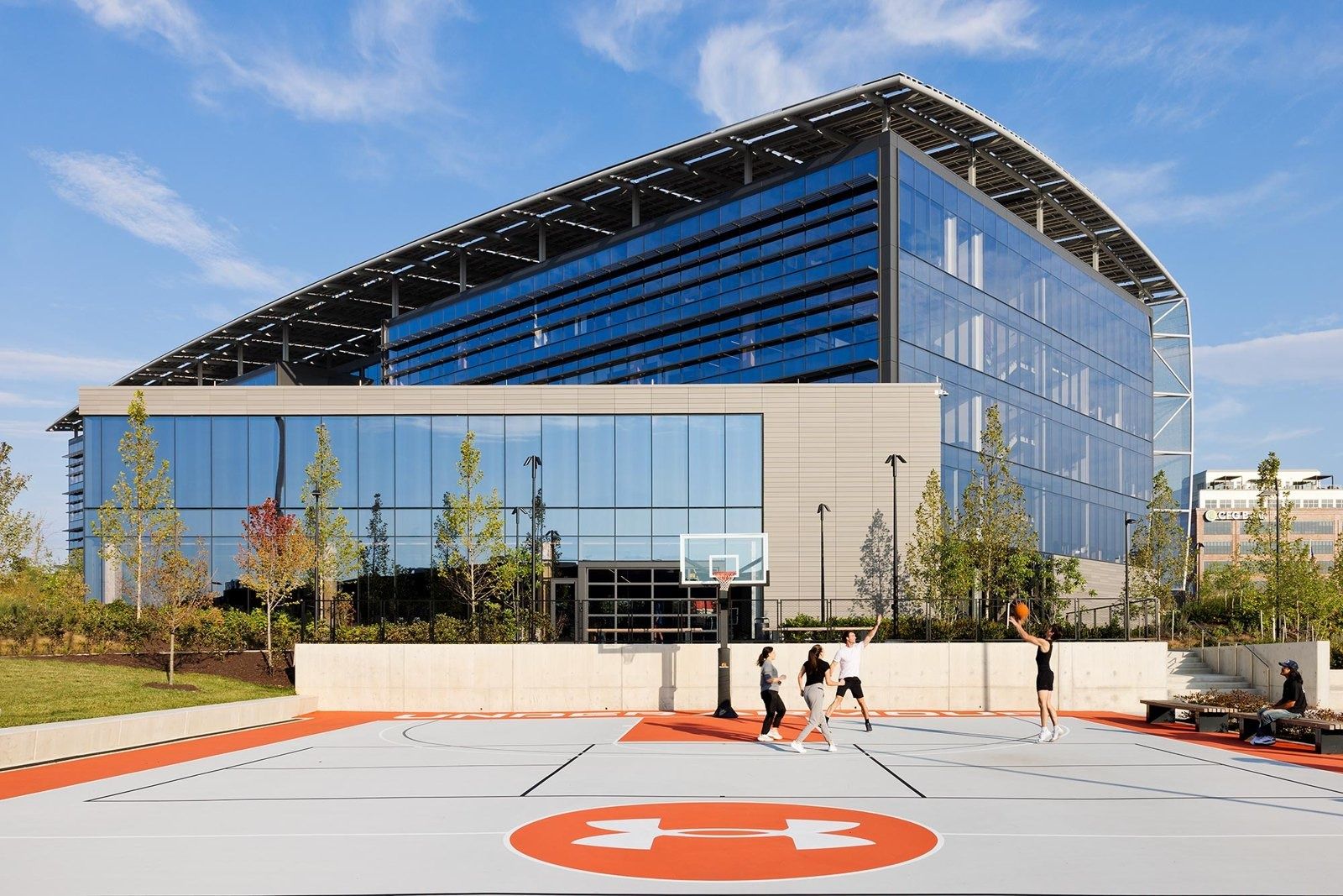 Under Armour: Outdoor basketball court with a logo at centre court in front of the glass headquarters building