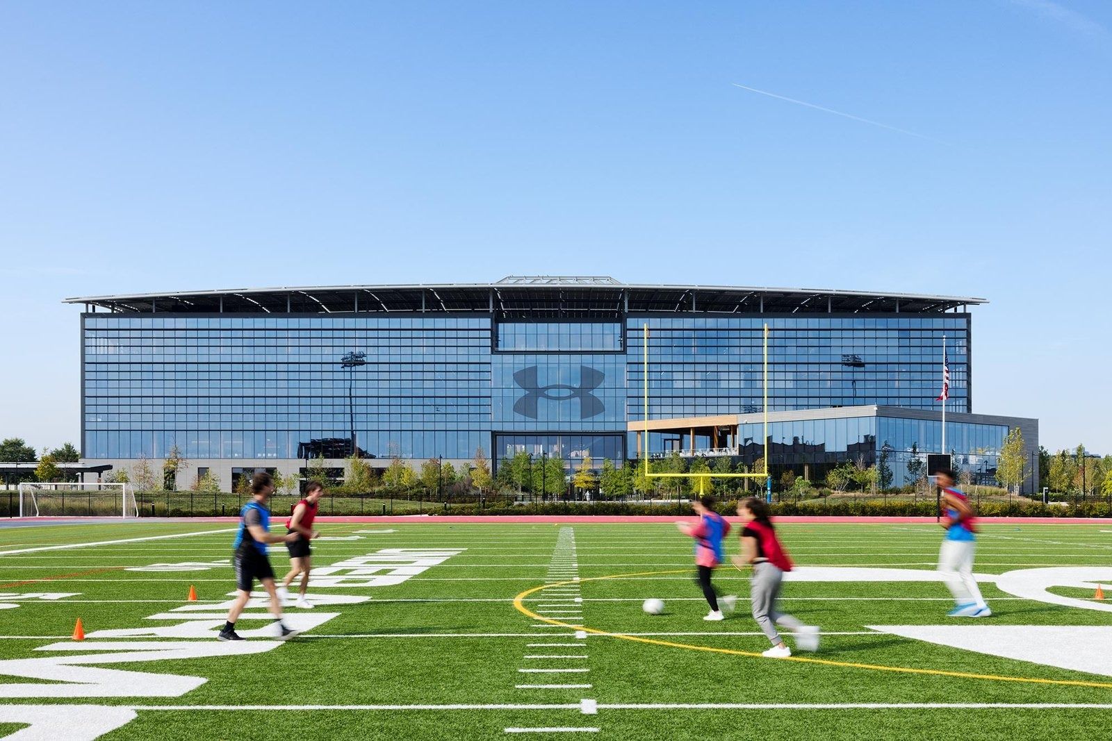 Under Armour: People playing football on a turf field in front of a glass office building