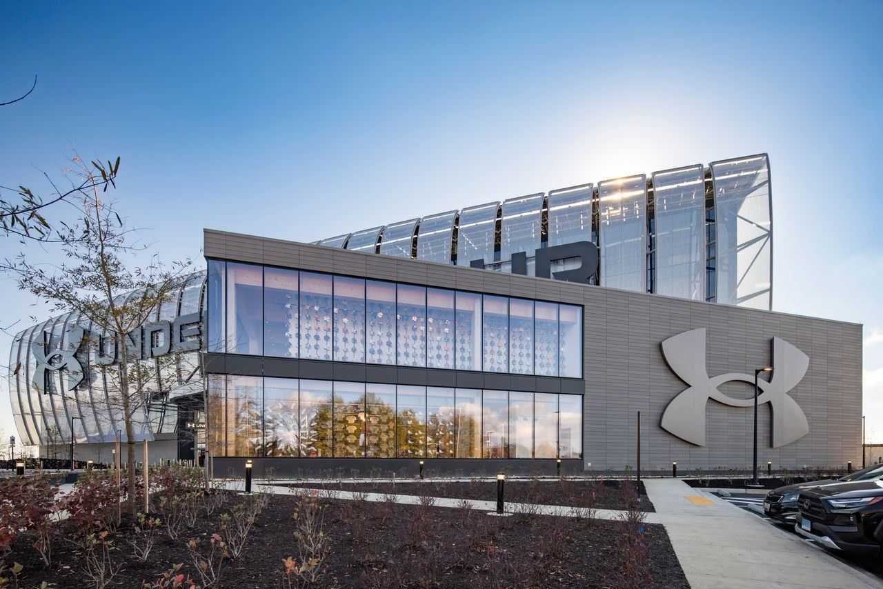 Under Armour: Store building with a large logo on a grey wall and tall windows, curved headquarters facade behind