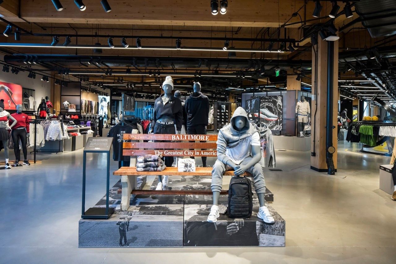 Under Armour: Store floor with mannequins seated on a bench display and racks of clothing beyond