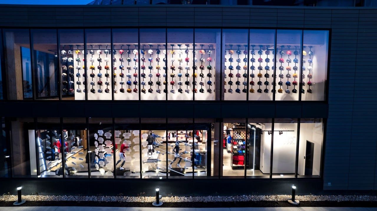 Under Armour: Store front at dusk with rows of lit display shelves visible through the windows